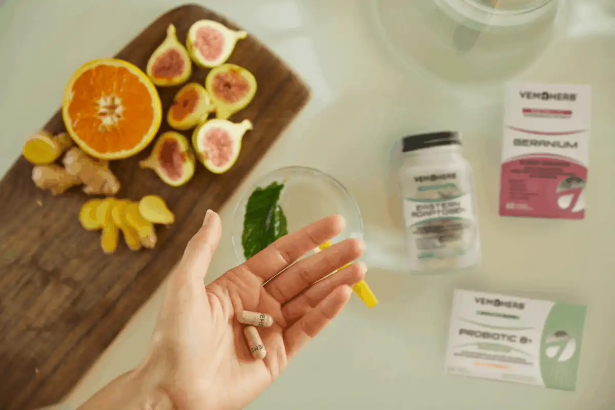Hand holding capsules with fruit, ginger, and VemoHerb supplements on table.